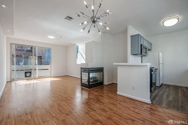 unfurnished living room featuring baseboards, visible vents, wood finished floors, and an inviting chandelier