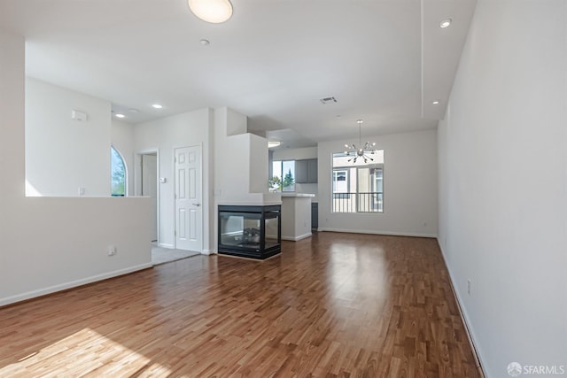 unfurnished living room featuring recessed lighting, baseboards, a chandelier, and wood finished floors