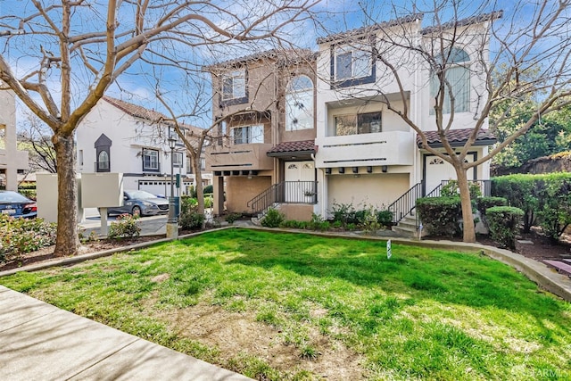 townhome / multi-family property with a tile roof, a front yard, stucco siding, and a balcony
