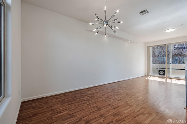 empty room with baseboards, visible vents, a chandelier, and wood finished floors
