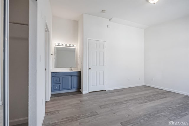 unfurnished bedroom featuring a sink, connected bathroom, baseboards, and wood finished floors