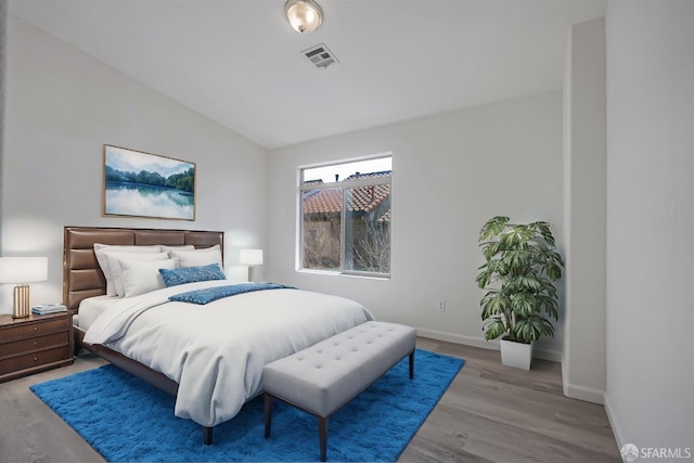 bedroom with baseboards, visible vents, vaulted ceiling, and wood finished floors