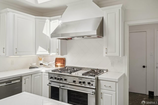 kitchen with appliances with stainless steel finishes, decorative backsplash, wall chimney range hood, and white cabinets