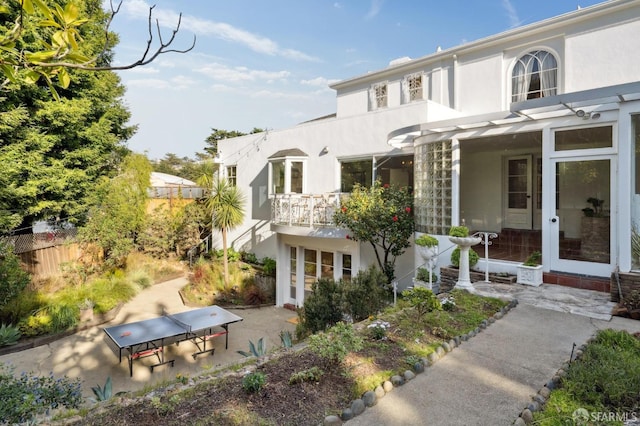 view of front facade with a balcony, fence, french doors, stucco siding, and a patio area