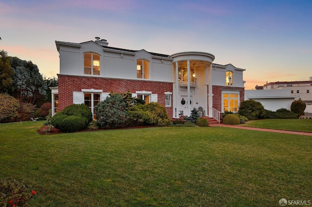 view of front of home featuring brick siding, a yard, and stucco siding