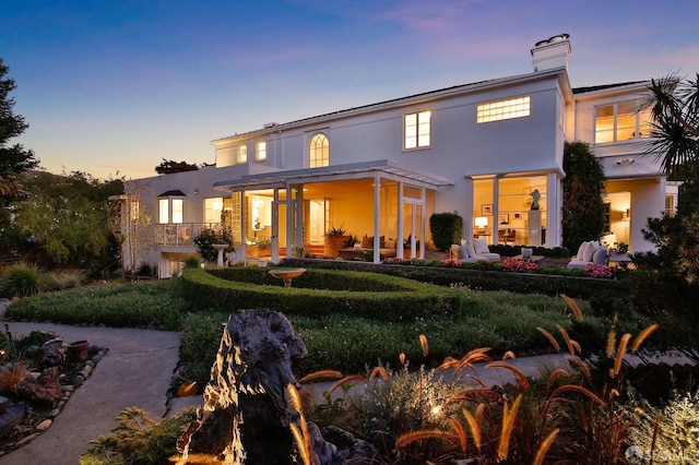 back of property at dusk featuring a chimney and stucco siding