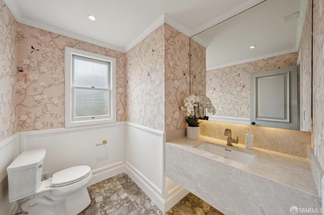 bathroom featuring wallpapered walls, a sink, and a wainscoted wall