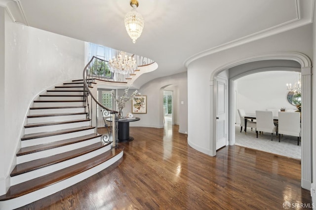 entrance foyer with arched walkways, wood finished floors, plenty of natural light, and an inviting chandelier