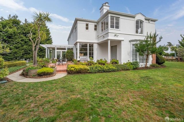 rear view of property featuring a chimney, a pergola, a lawn, and stucco siding