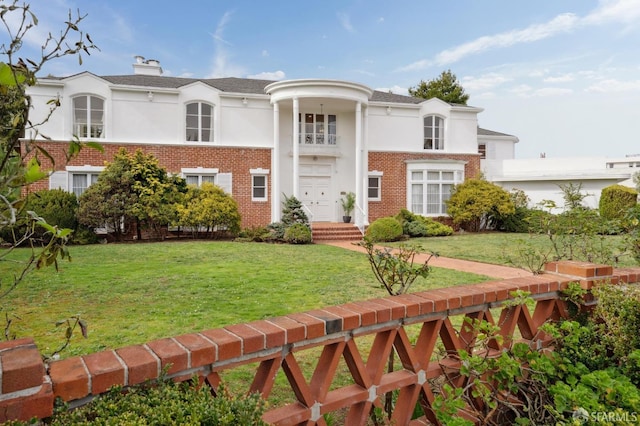 view of front of property featuring stucco siding, a front yard, a chimney, and brick siding