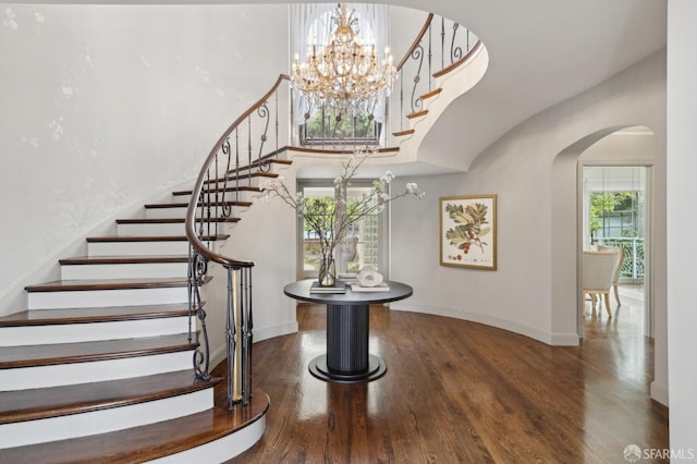 stairway with baseboards, a high ceiling, arched walkways, and wood finished floors