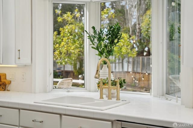 kitchen featuring tile counters, backsplash, white cabinets, a sink, and dishwashing machine