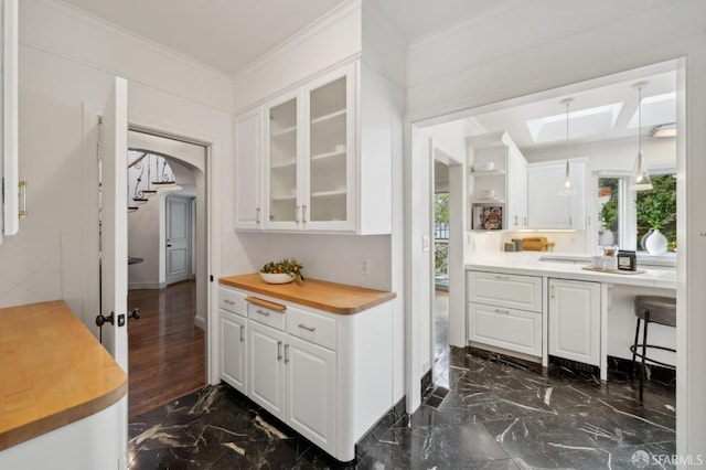 kitchen featuring butcher block countertops, marble finish floor, white cabinetry, and ornamental molding