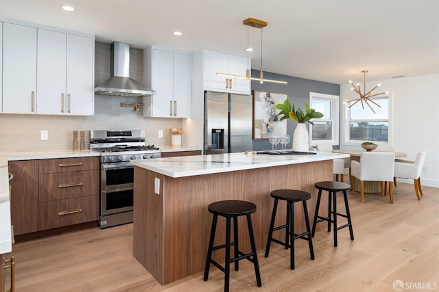 2277 33rd Ave, San Francisco, CA 94116 - kitchen with wall chimney range hood, appliances with stainless steel finishes, light wood-type flooring, a chandelier, and a kitchen bar