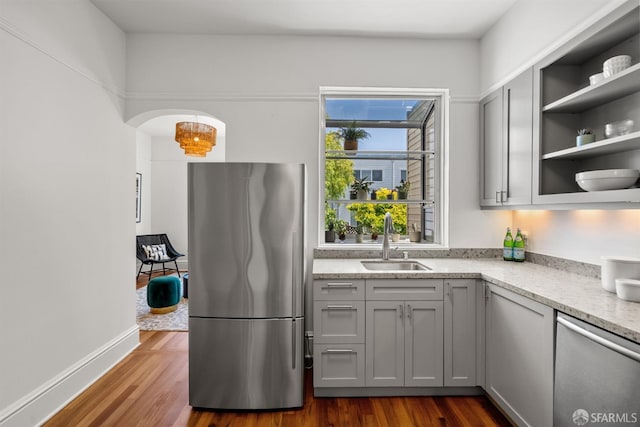 kitchen featuring stainless steel appliances, a sink, gray cabinets, dark wood-style floors, and open shelves