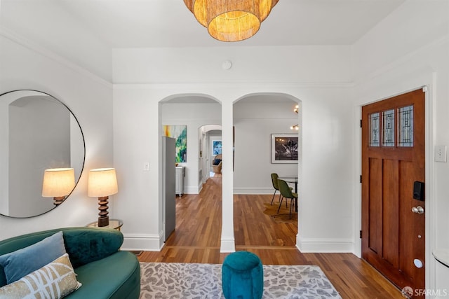 foyer with arched walkways, wood finished floors, and baseboards