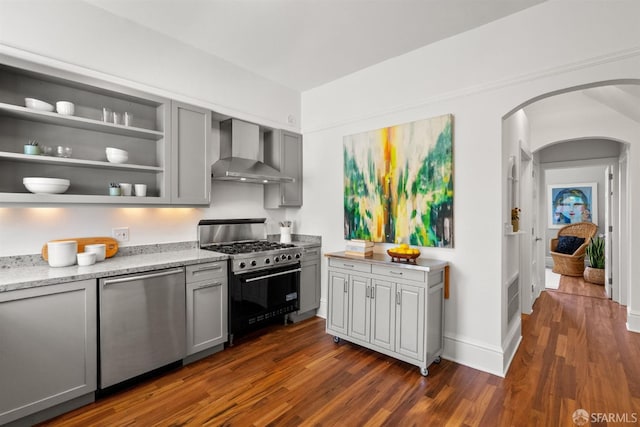 kitchen featuring wall chimney range hood, stainless steel appliances, gray cabinetry, and arched walkways