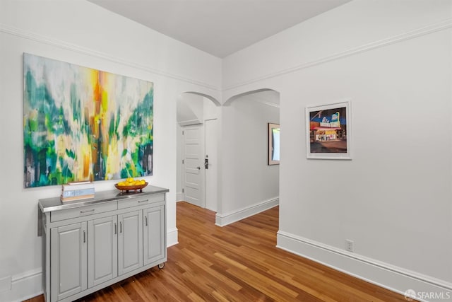 corridor with arched walkways, wood finished floors, and baseboards