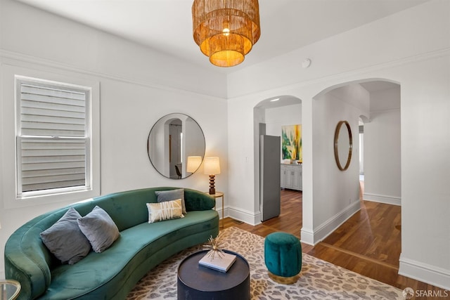 living area with wood finished floors, arched walkways, and baseboards
