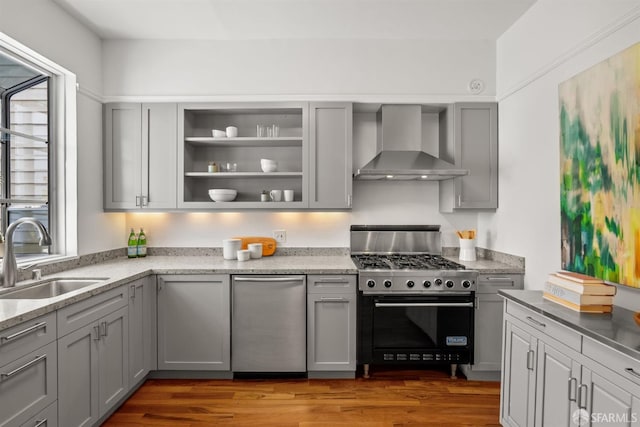 kitchen featuring wall chimney range hood, high end stainless steel range oven, a sink, gray cabinetry, and healthy amount of natural light