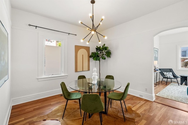 dining room with wood finished floors, arched walkways, a chandelier, and baseboards