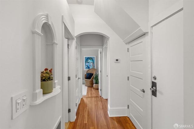 hall featuring light wood-style flooring, baseboards, and arched walkways