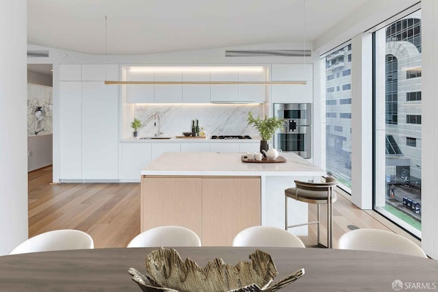 kitchen featuring light hardwood / wood-style floors, stainless steel double oven, white cabinets, lofted ceiling, and sink