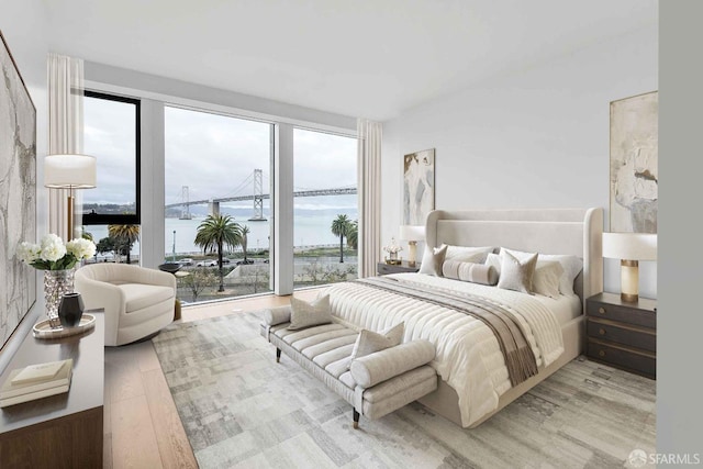 bedroom featuring multiple windows, access to exterior, light wood-type flooring, and a water view