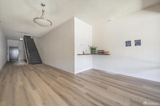 unfurnished living room with vaulted ceiling, a textured ceiling, and light wood-type flooring