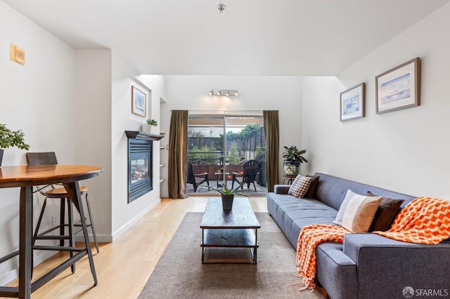 living area with light wood finished floors, a glass covered fireplace, and baseboards