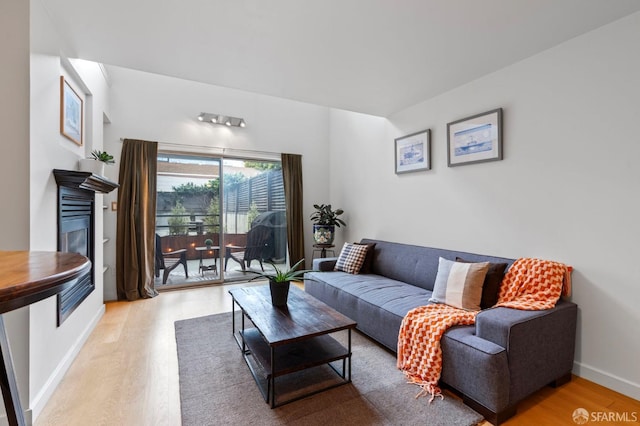 living room featuring light wood-style floors, a glass covered fireplace, and baseboards