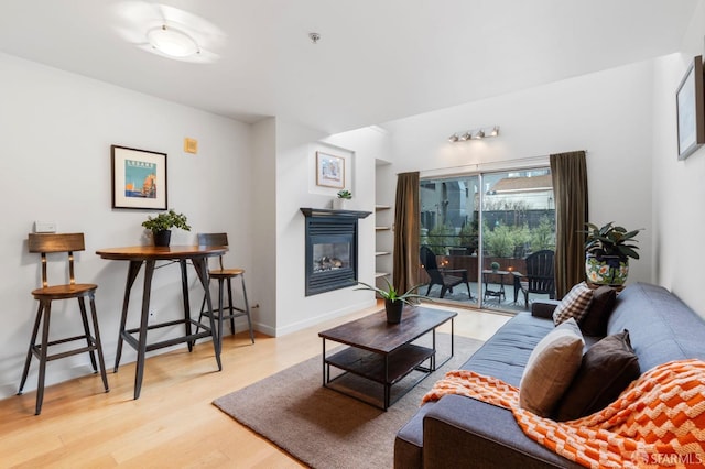 living area featuring a glass covered fireplace, wood finished floors, and built in shelves