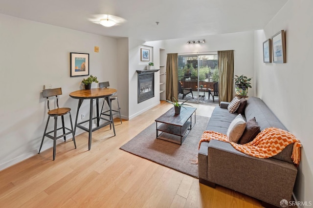 living area with a glass covered fireplace, wood finished floors, and baseboards