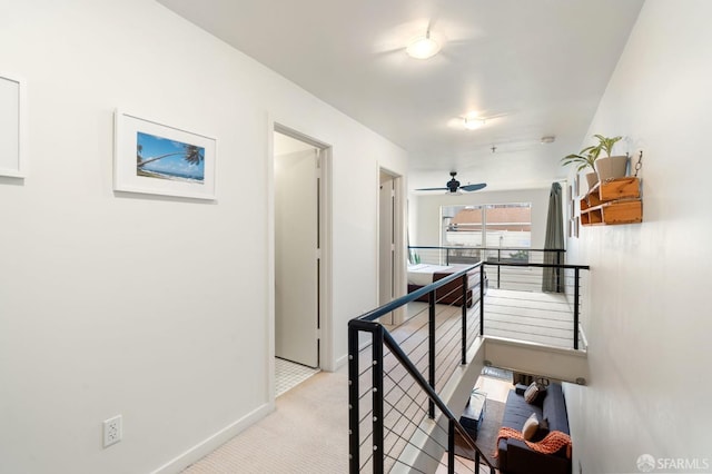 hallway with an upstairs landing, light colored carpet, and baseboards