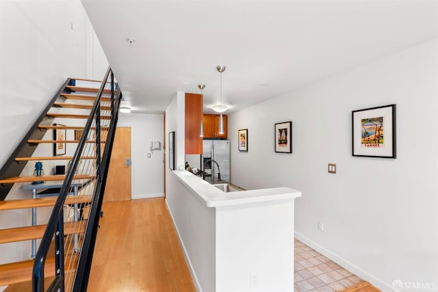 kitchen featuring stainless steel fridge, a peninsula, a sink, baseboards, and light wood-type flooring