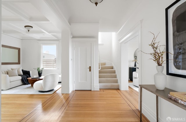 foyer entrance with light wood-style floors, stairs, coffered ceiling, and beamed ceiling