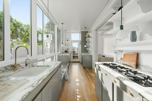 kitchen featuring light stone counters, gray cabinets, a sink, and light wood-style flooring