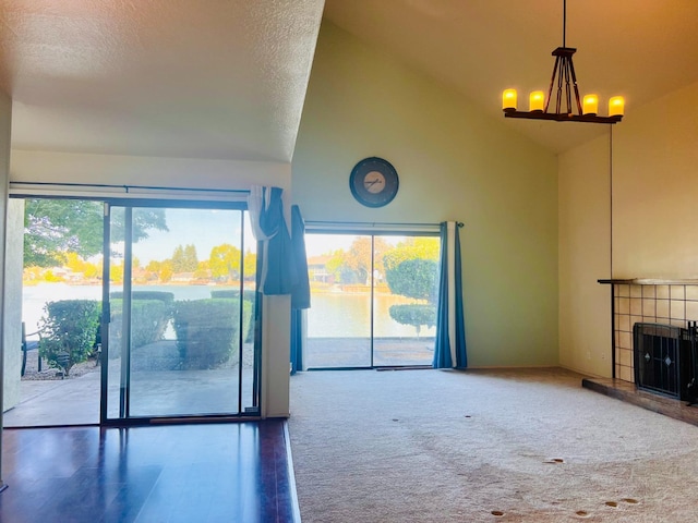 unfurnished living room featuring a textured ceiling, high vaulted ceiling, carpet flooring, a tile fireplace, and a notable chandelier