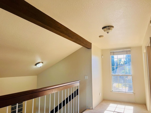 corridor featuring light carpet, a textured ceiling, and vaulted ceiling with beams