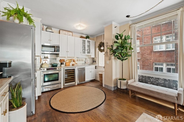 kitchen featuring a wealth of natural light, appliances with stainless steel finishes, ornamental molding, white cabinets, and beverage cooler