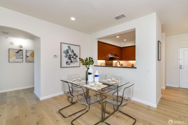 dining area with visible vents, light wood finished floors, baseboards, recessed lighting, and arched walkways