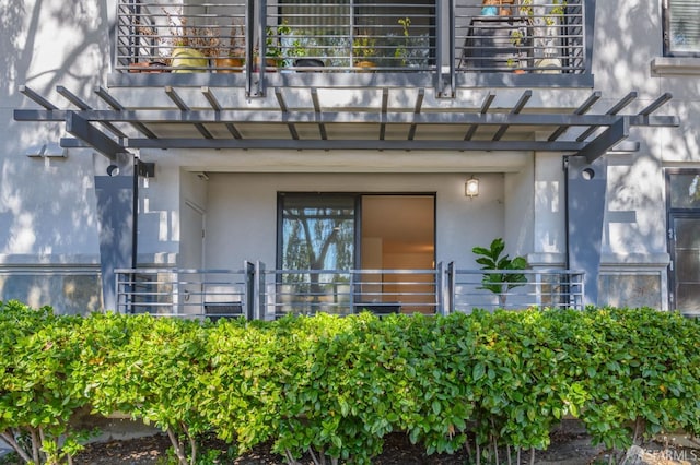 view of exterior entry featuring a balcony and stucco siding