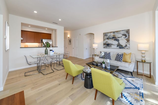 living area with visible vents, baseboards, light wood-style flooring, recessed lighting, and arched walkways