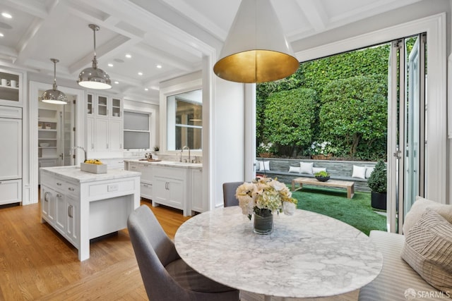 dining space featuring sink, coffered ceiling, light wood-type flooring, and beam ceiling