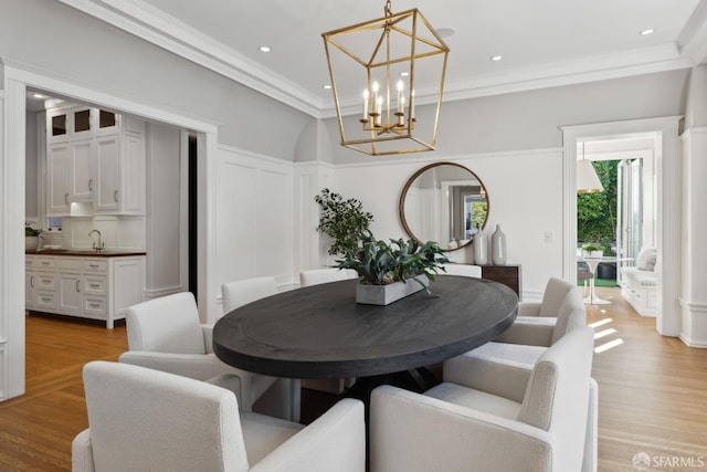 dining space featuring sink, light hardwood / wood-style flooring, ornamental molding, and an inviting chandelier