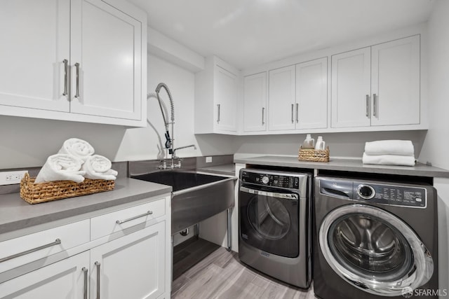 clothes washing area with cabinets, separate washer and dryer, light hardwood / wood-style flooring, and sink