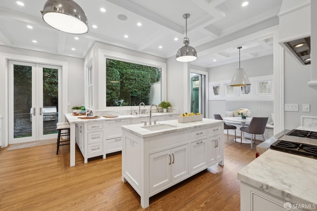 kitchen featuring hanging light fixtures, sink, white cabinets, a kitchen island with sink, and light hardwood / wood-style floors