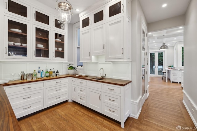 kitchen featuring white cabinetry, sink, light wood-type flooring, pendant lighting, and butcher block countertops