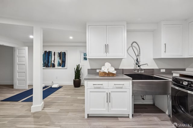 kitchen with sink, white cabinets, light wood-type flooring, and washer / clothes dryer