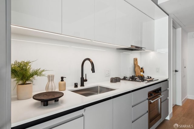 kitchen with backsplash, white cabinets, sink, light hardwood / wood-style flooring, and stainless steel appliances